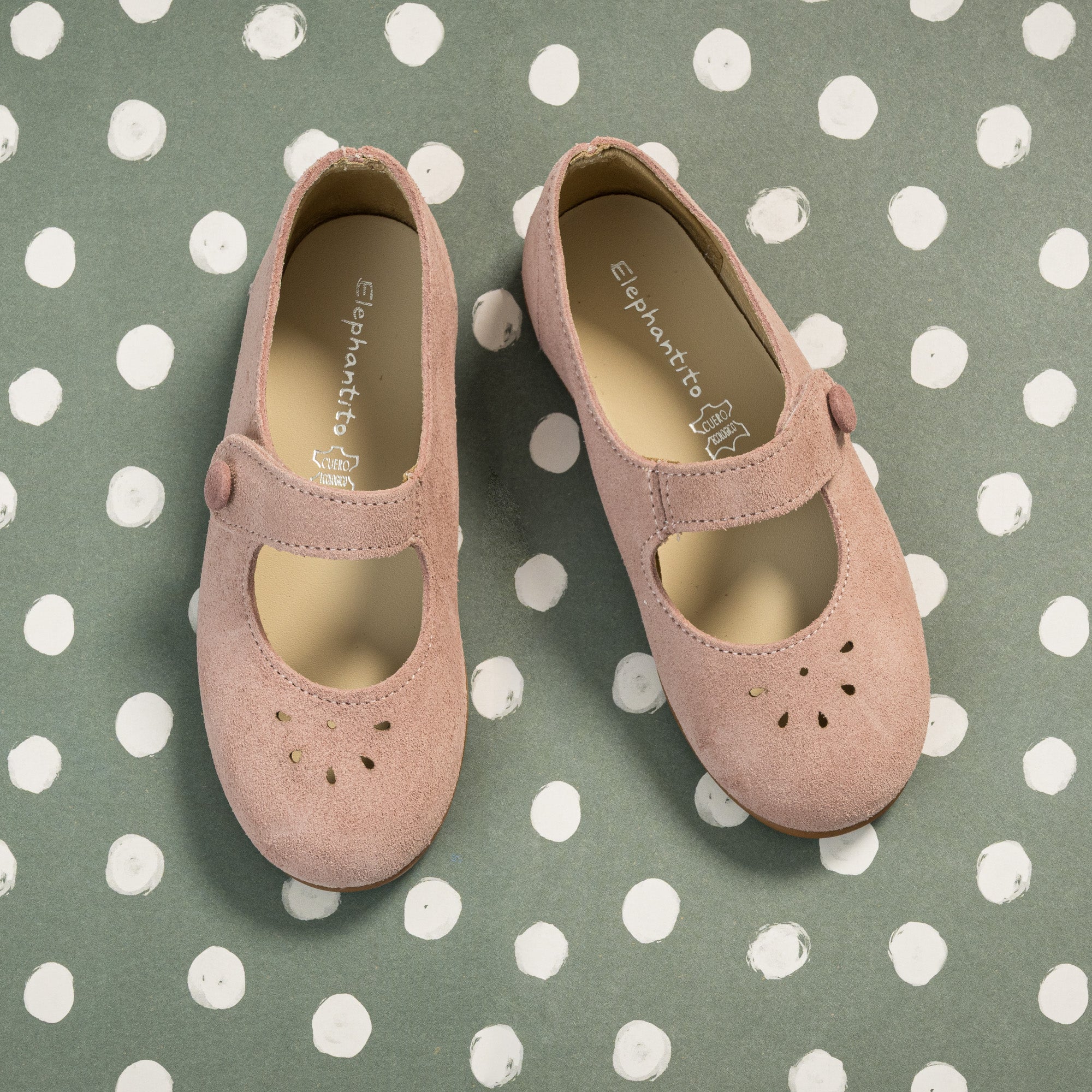Pink suede Mary Jane shoes with perforated floral details and Velcro strap for toddlers.