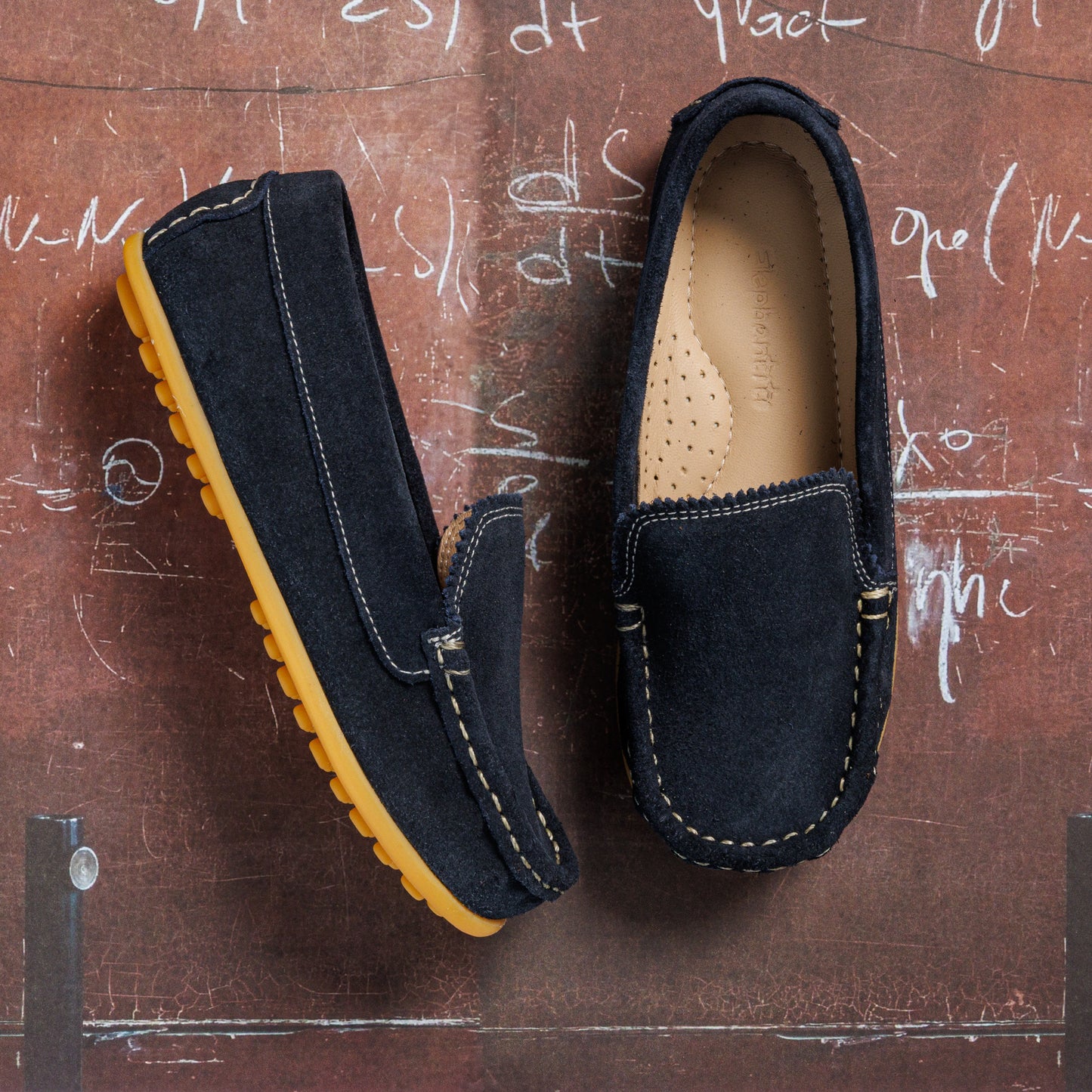 Navy blue suede toddler moccasin shoes with tan rubber soles and white stitching details.