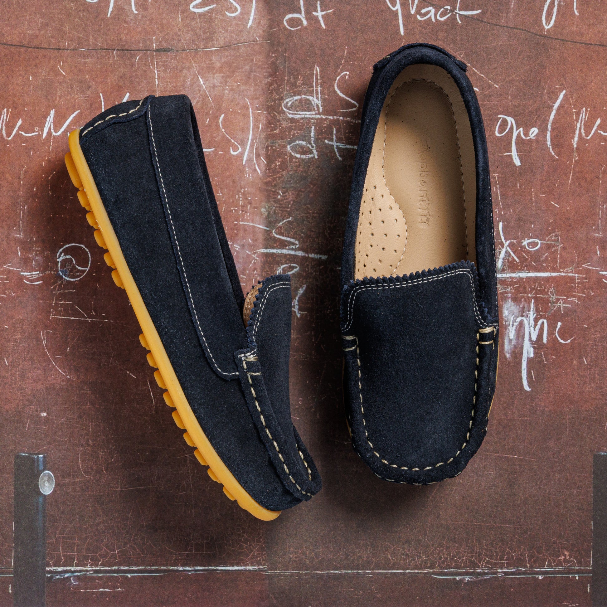Navy blue suede toddler moccasin shoes with tan rubber soles and white stitching details.