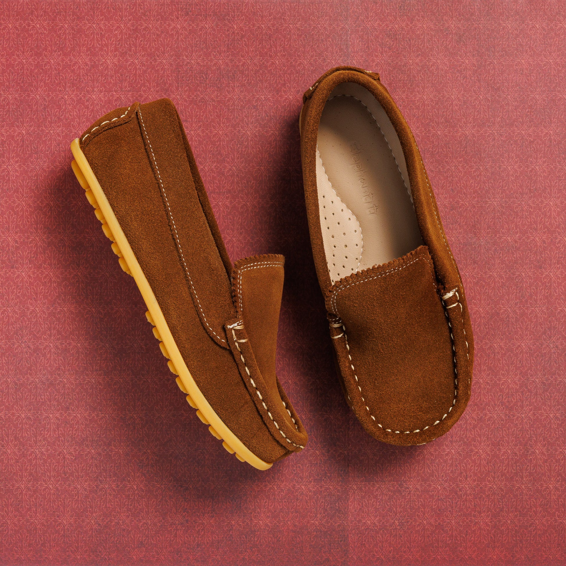 Chestnut brown suede moccasin-style children's shoes with stitched detailing and tan rubber soles.