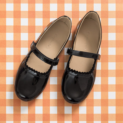 Black patent leather Mary Jane flats with scalloped edges and adjustable straps for children.