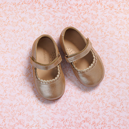 Blush pink toddler Mary Jane shoes with scalloped edges and velcro strap on floral background.