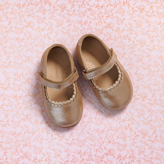 Blush pink toddler Mary Jane shoes with scalloped edges and velcro strap on floral background.