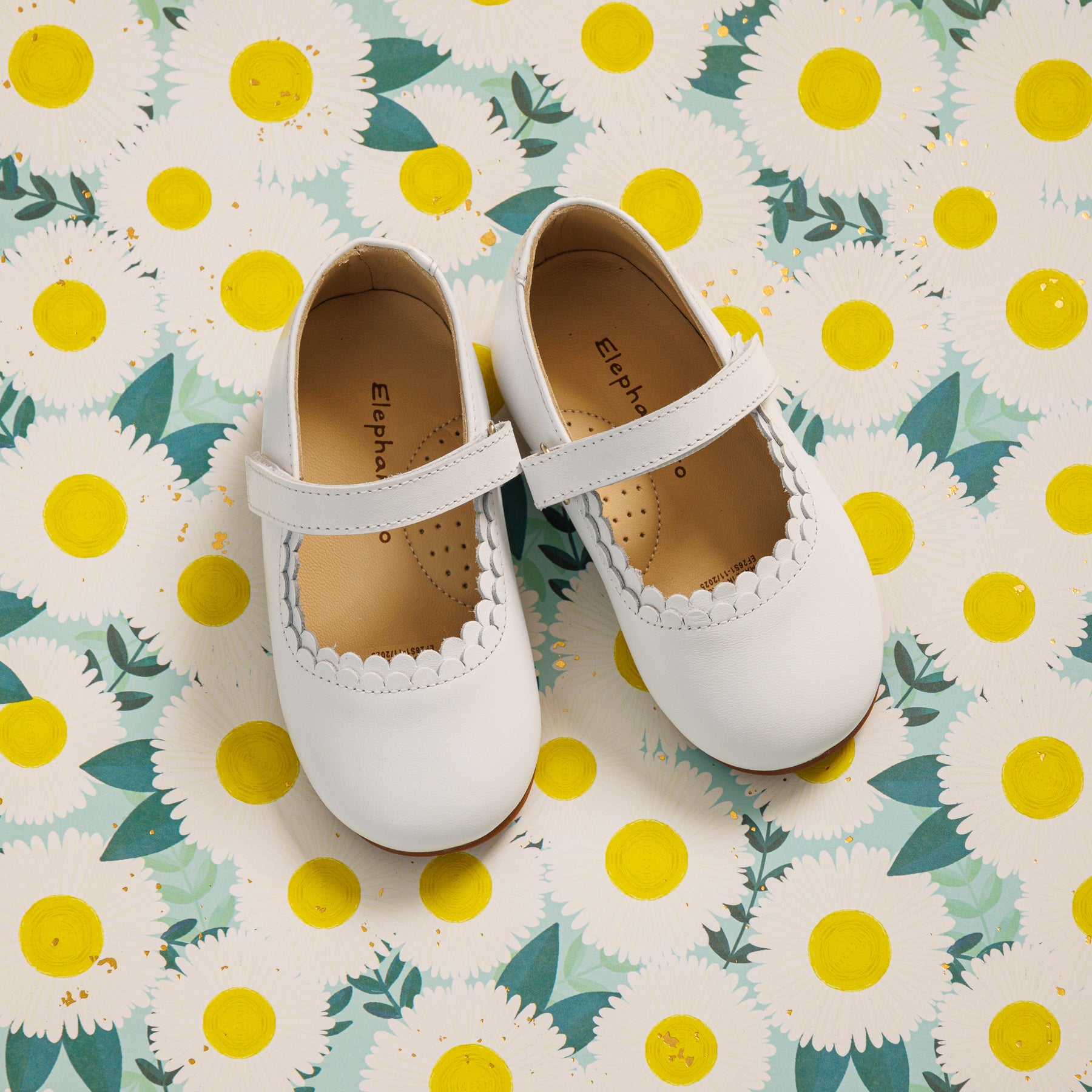 Elephantito - White toddler Mary Jane shoes with scalloped edges and single Velcro strap on floral background.