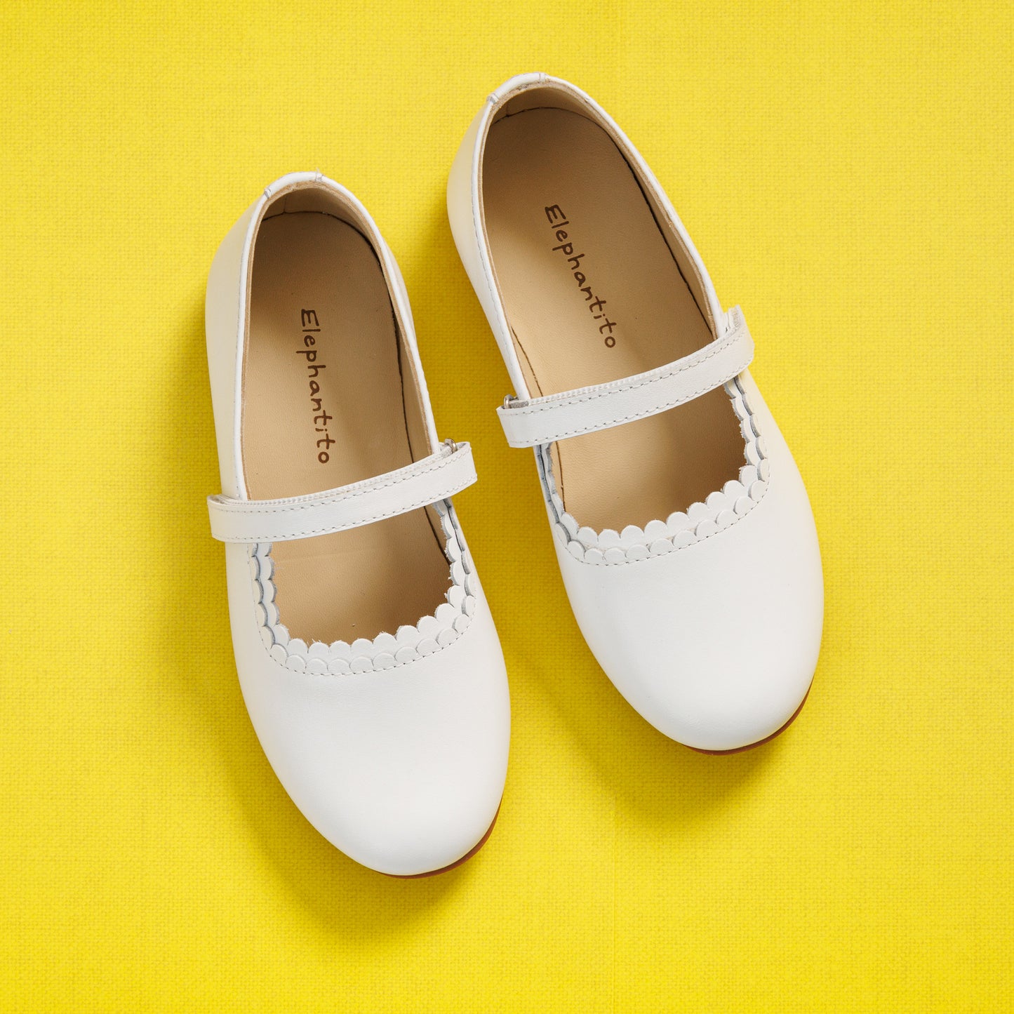 Elephantito - White toddler girl Mary Jane shoes with scalloped edge and single strap on yellow background.