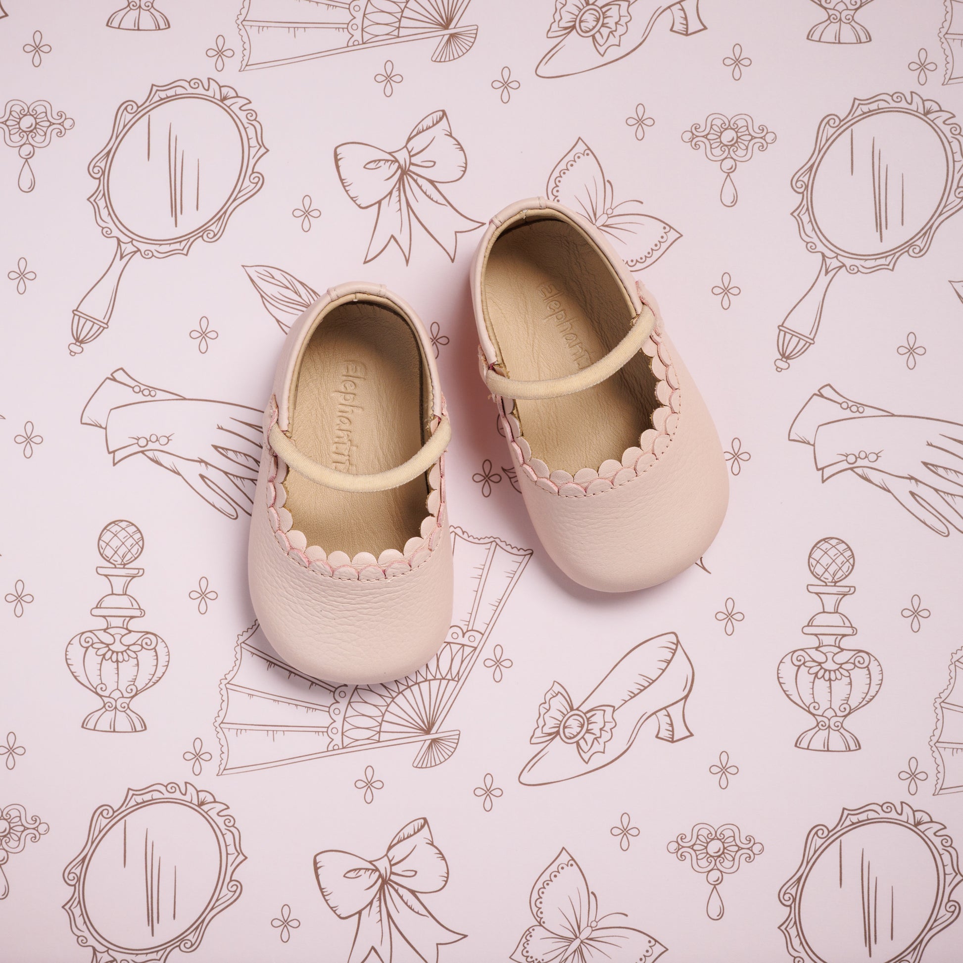 Soft pink toddler ballet shoes with scalloped trim and Mary Jane strap on decorative pink background.