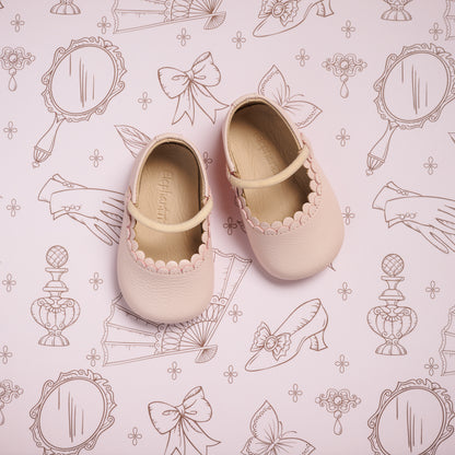 Soft pink toddler ballet shoes with scalloped trim and Mary Jane strap on decorative pink background.