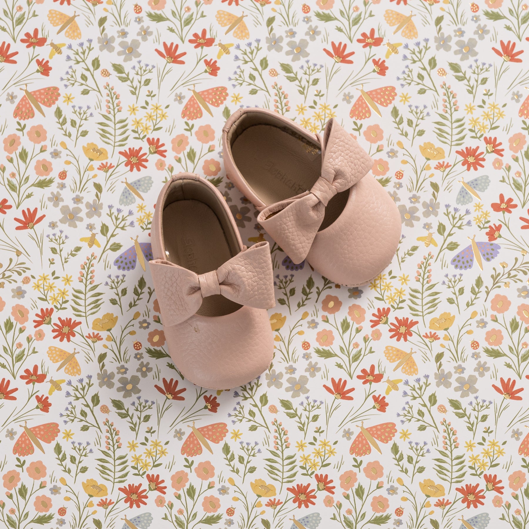 Soft pink baby ballerina shoes with large textured bows on top, made from smooth material.