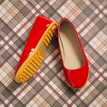 Red patent leather toddler ballerina flats with beige interior and textured yellow rubber sole.