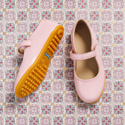 Pink toddler Mary Jane shoes with adjustable strap and textured rubber sole on patterned background.