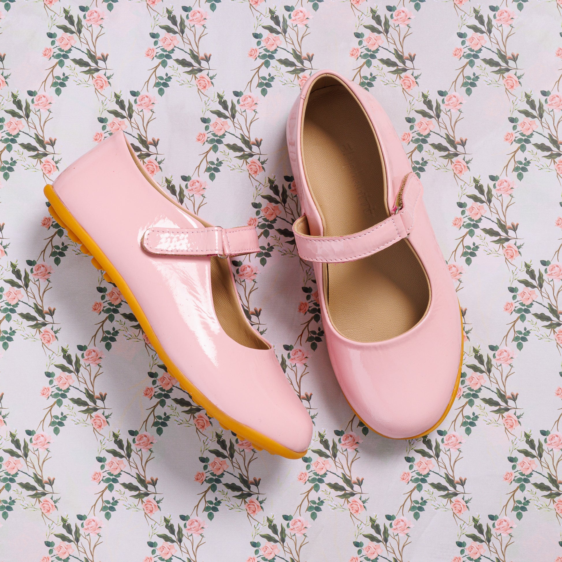 Glossy light pink toddler Mary Jane shoes with a strap and rubber sole on floral background.