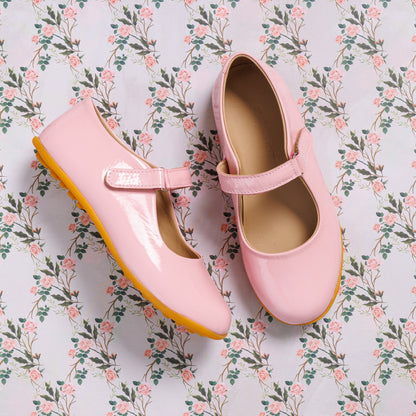 Glossy light pink toddler Mary Jane shoes with a strap and rubber sole on floral background.