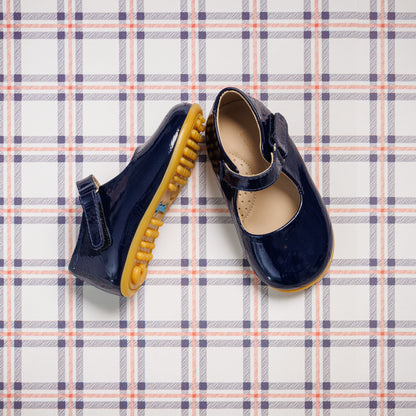Navy blue patent leather toddler Mary Jane shoes with rounded toes and yellow rubber soles on plaid background.
