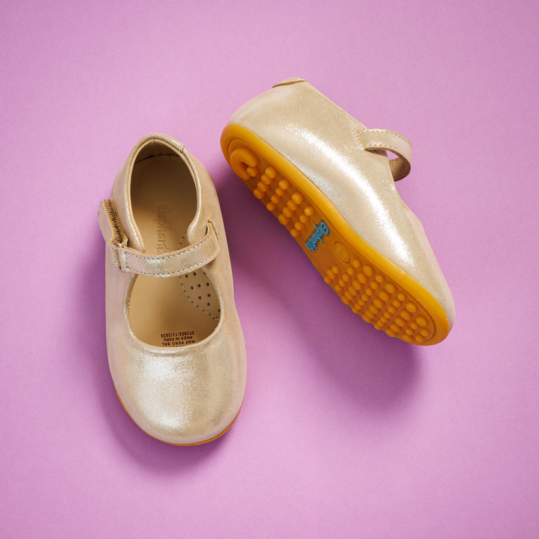 Elephantito - Metallic beige toddler Mary Jane shoes with adjustable strap and textured orange sole on pink background.
