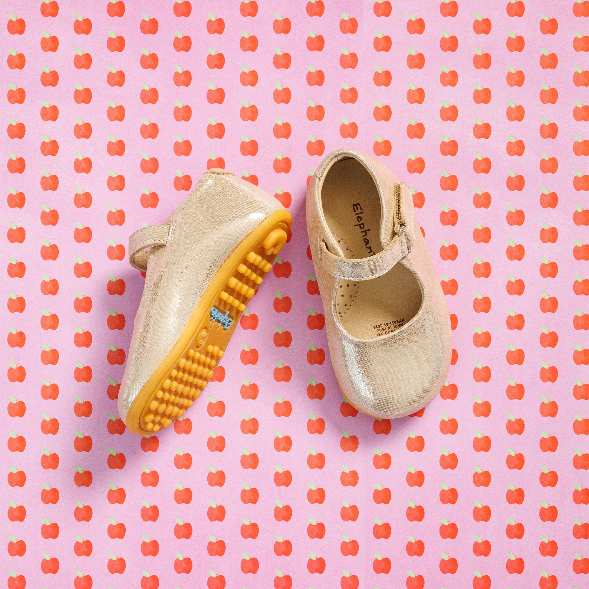 Elephantito - Cream toddler Mary Jane shoes with yellow textured soles on pink apple-patterned background.