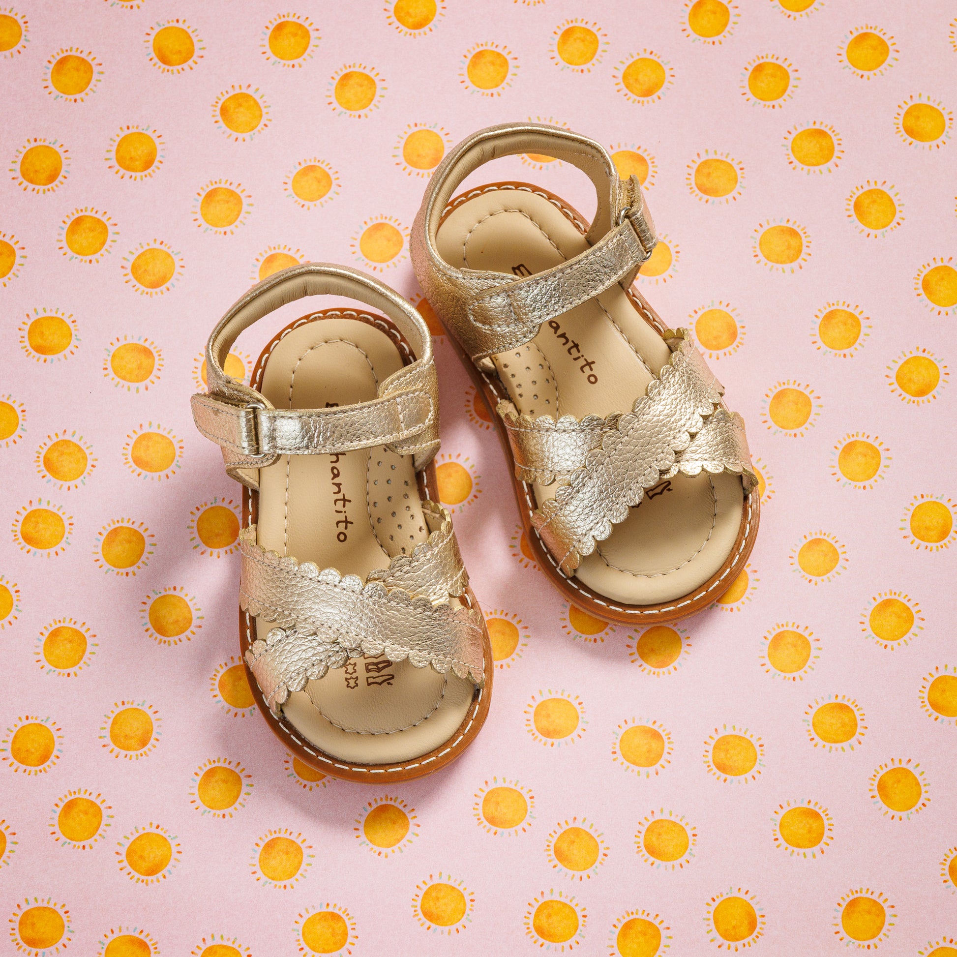 Elephantito - Gold toddler sandals with scalloped straps and adjustable ankle closures on polka dot background.