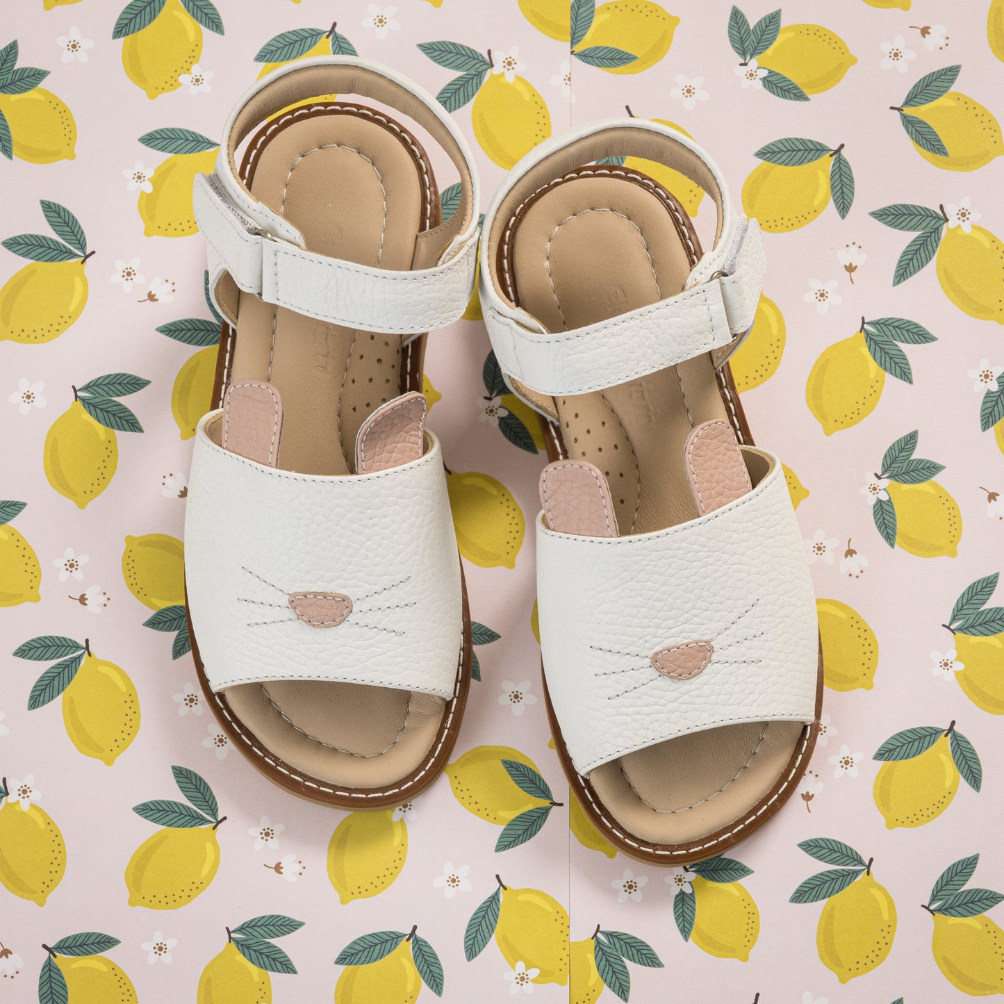 White toddler sandals with bunny face design and adjustable ankle straps on lemon-patterned background.