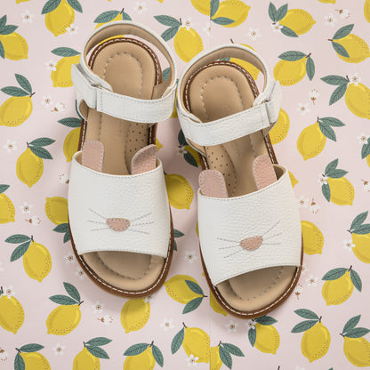 White toddler sandals with bunny face design and adjustable ankle straps on lemon-patterned background.