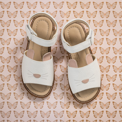 White toddler sandals with bunny face design and adjustable ankle straps on butterfly-patterned background.