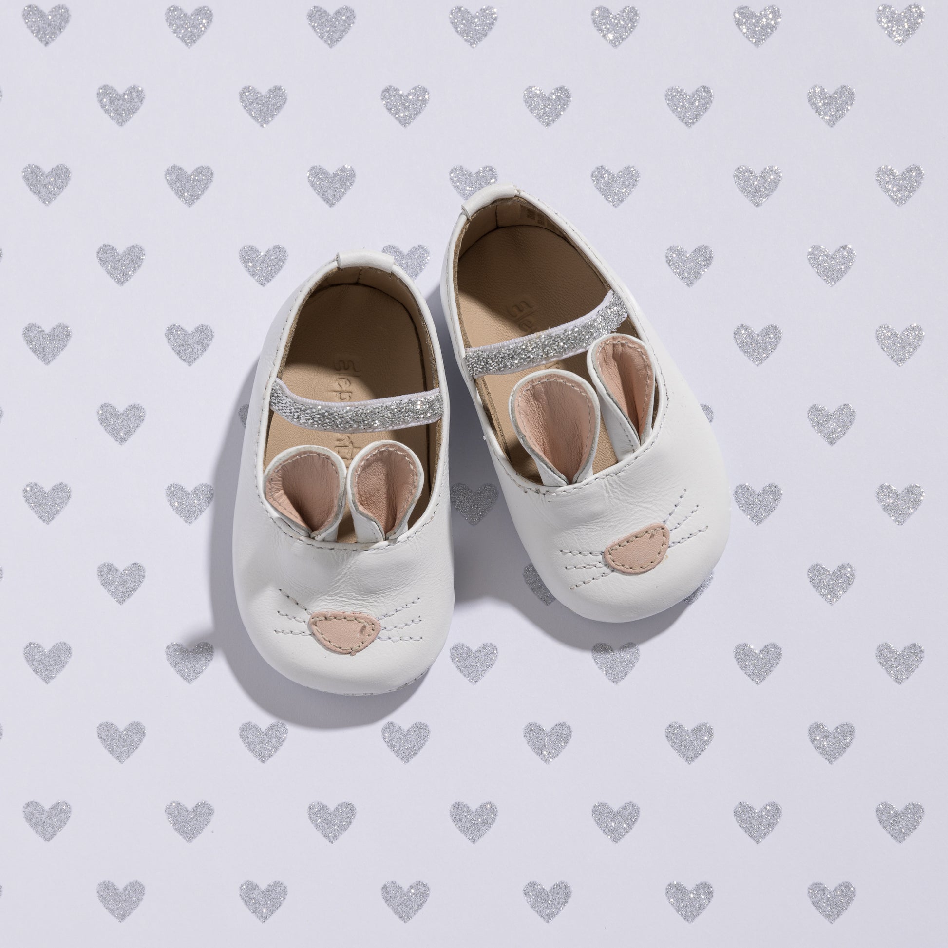 White baby slippers with soft fabric bunny ears and embroidered nose on top.