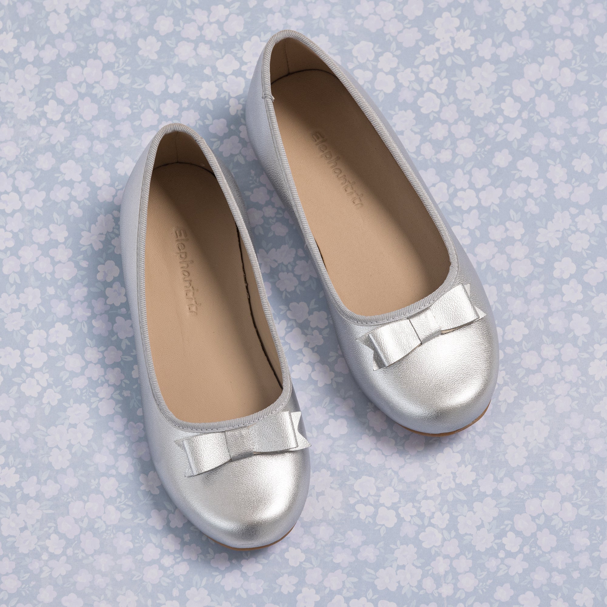 Silver toddler ballet flats with rounded toes and subtle bow accents on top.