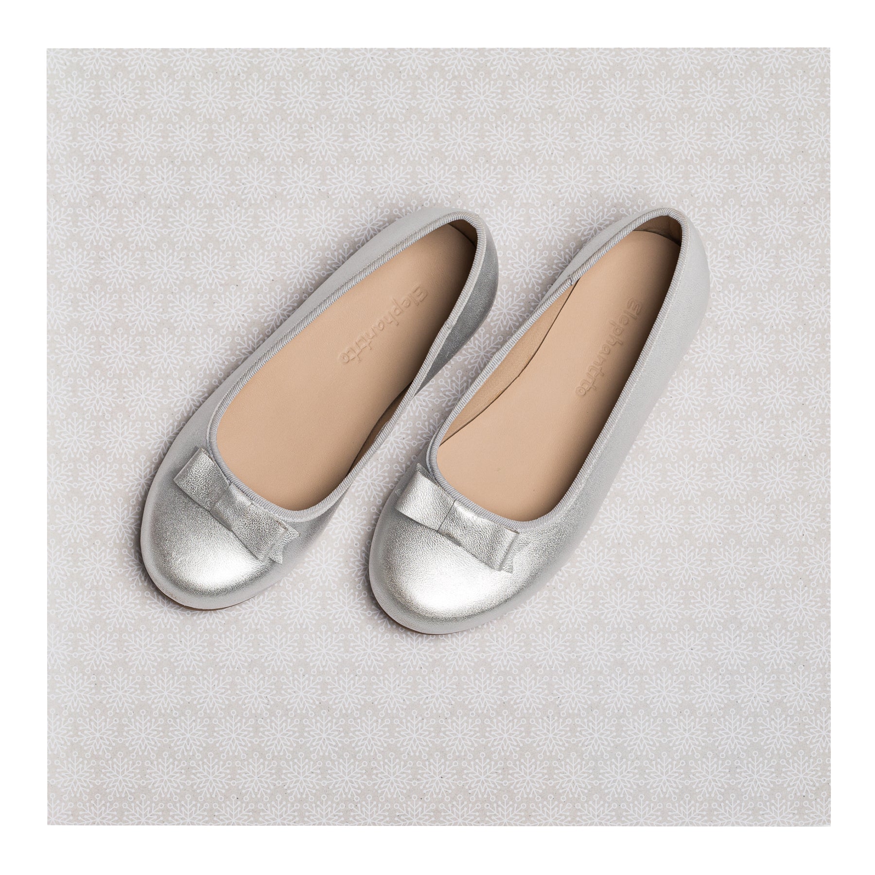 Silver metallic girls' ballet flats with rounded toes and a small bow detail on top.