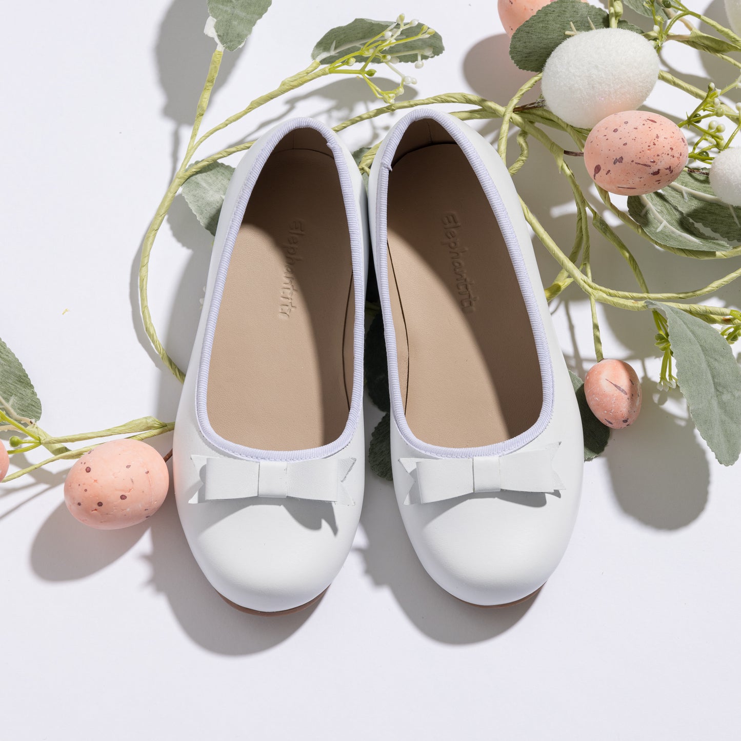 White toddler ballerina flats with rounded toes and small decorative bows on top.