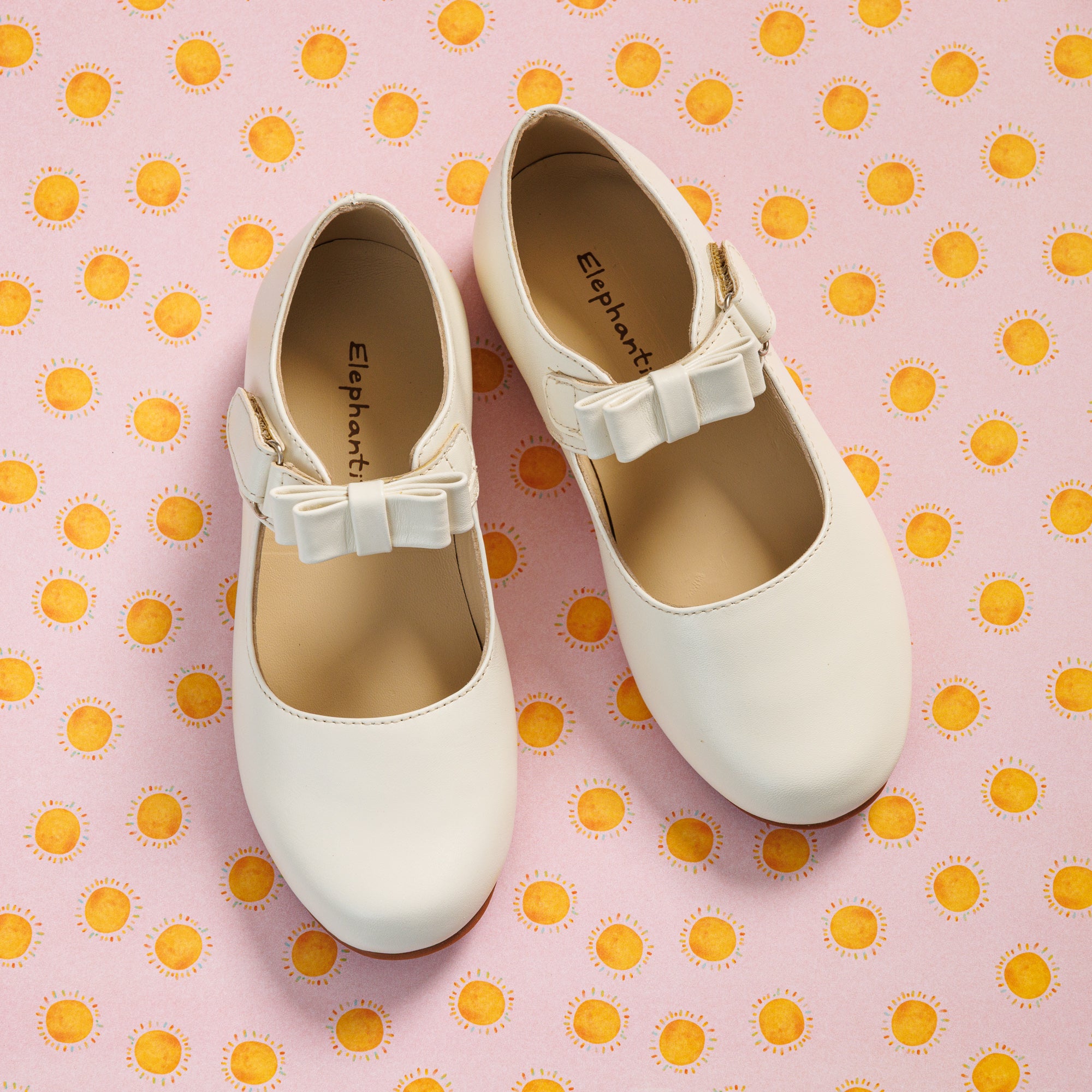 Elephantito - Bone white toddler Mary Jane shoes with a delicate bow and round toe on pink polka dot background.
