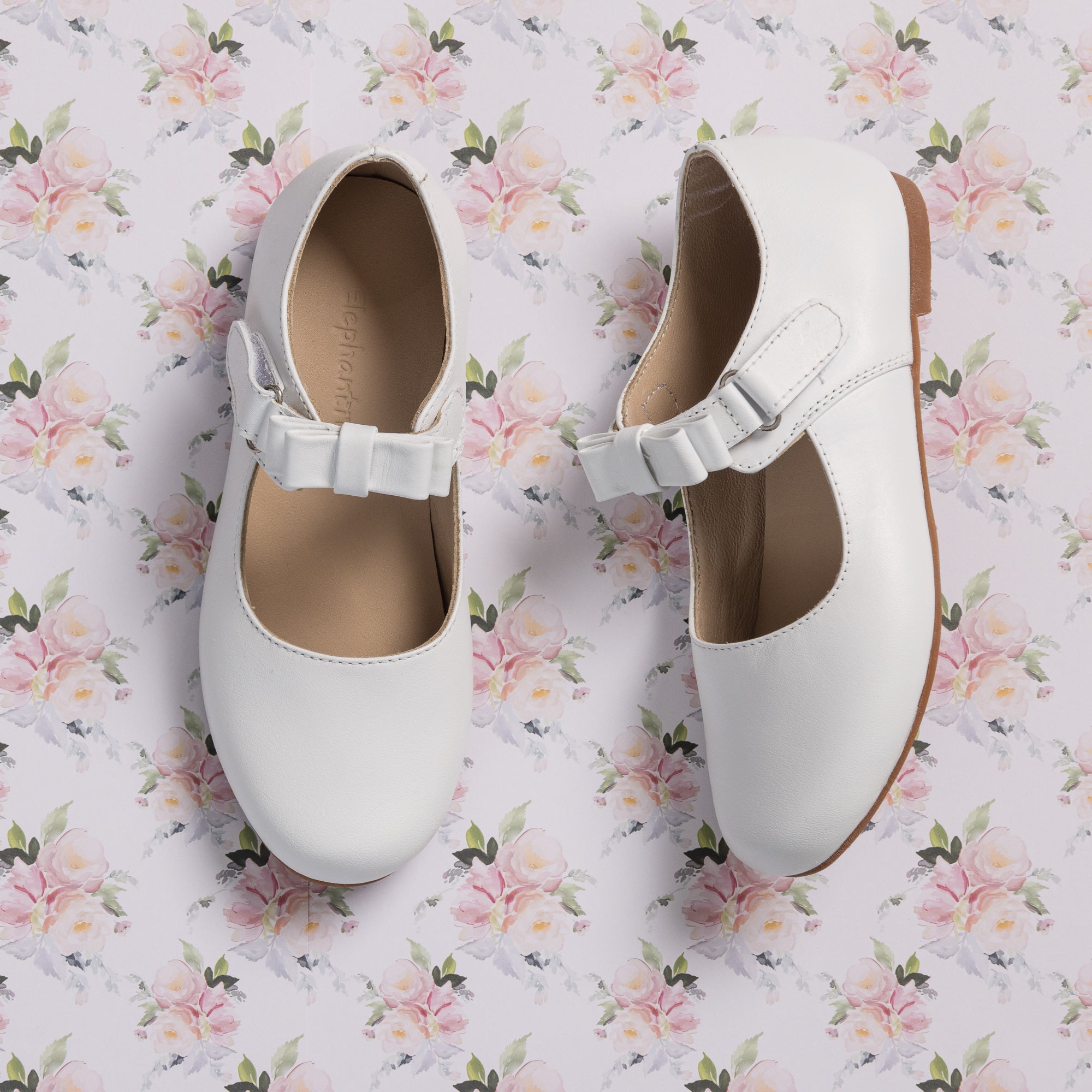 White leather Mary Jane shoes for girls with a strap and bow detail on floral background.