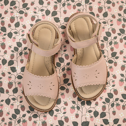 Pink toddler sandals with scalloped edges and ankle straps on floral background.