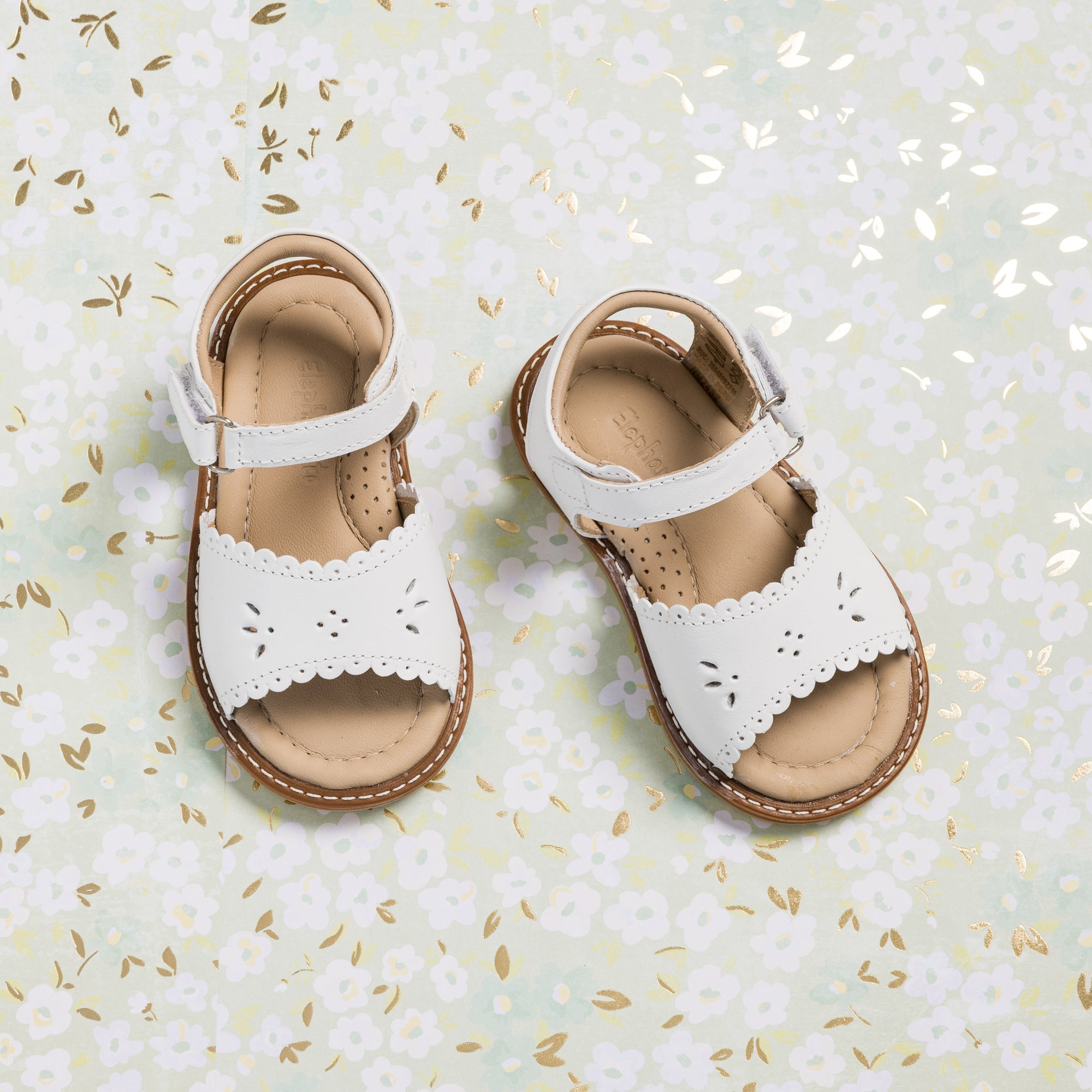 White toddler sandals with scalloped edges and floral cutout details on straps.