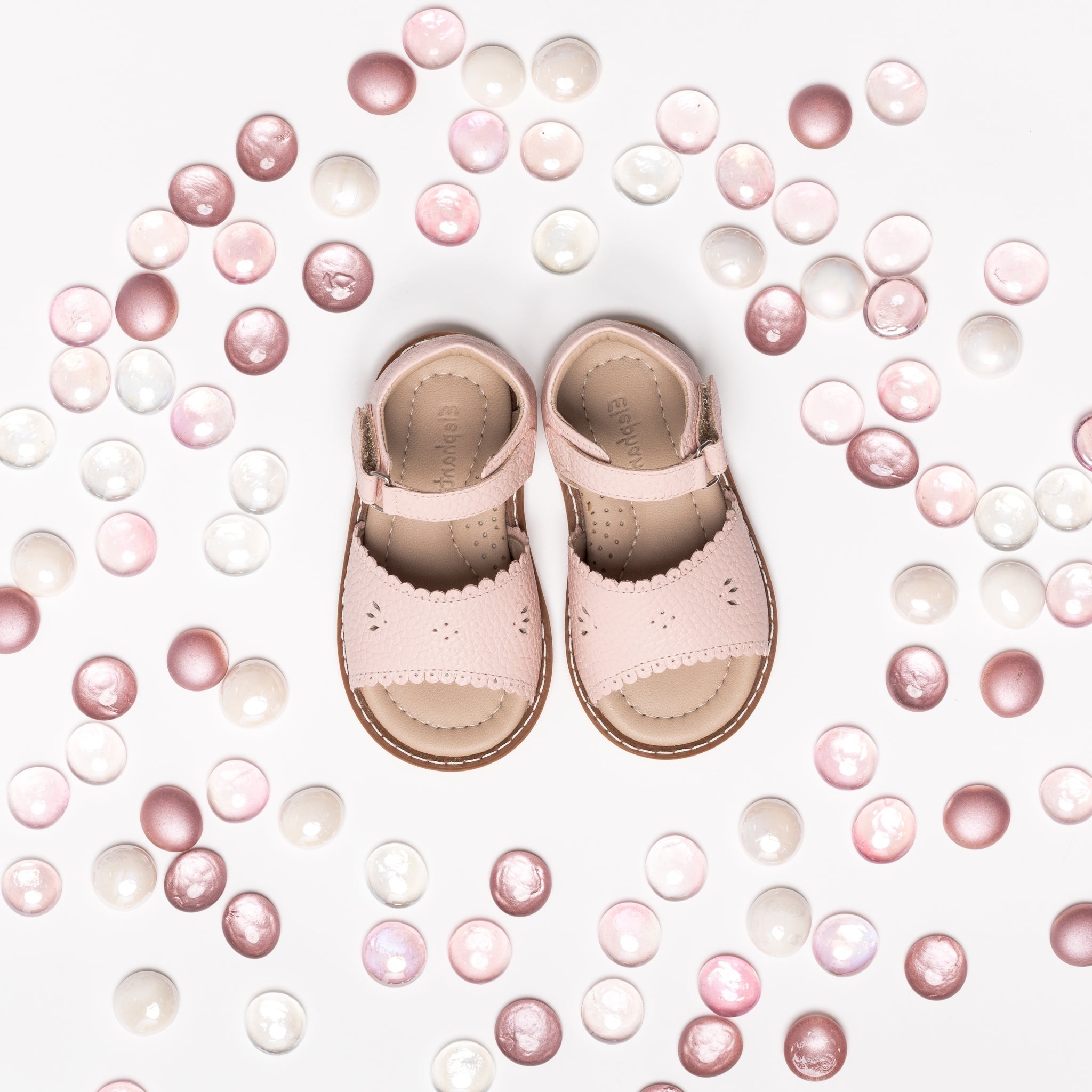 Pink toddler sandals with scalloped edges and ankle straps surrounded by pink and white beads.
