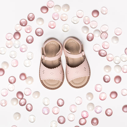 Pink toddler sandals with scalloped edges and ankle straps surrounded by pink and white beads.