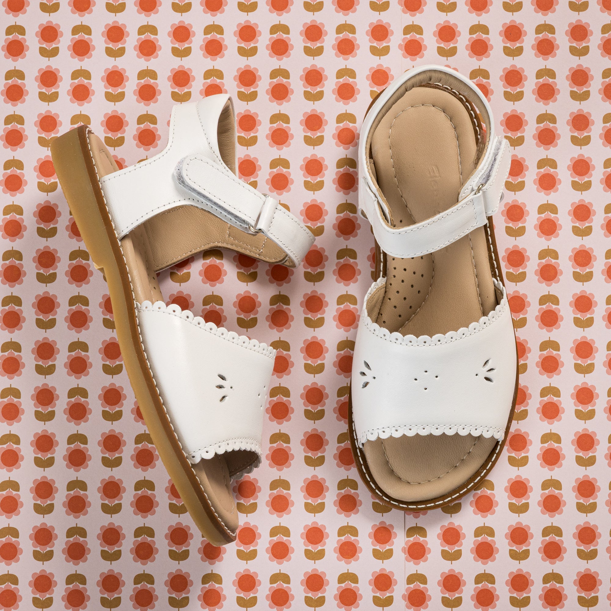 White toddler sandal with scalloped edges and perforated flower design on tan sole.