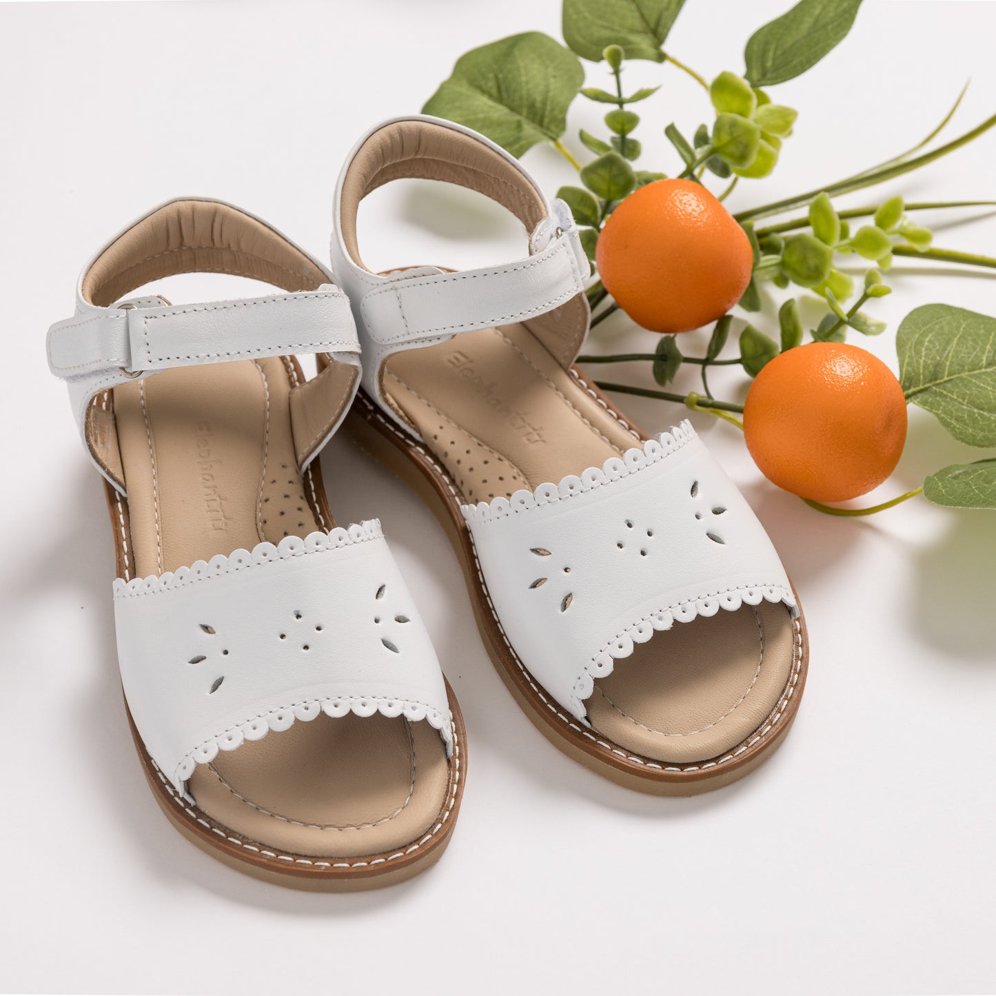 White toddler sandals with scalloped edges and butterfly cutouts, cushioned footbed, and Velcro ankle straps.