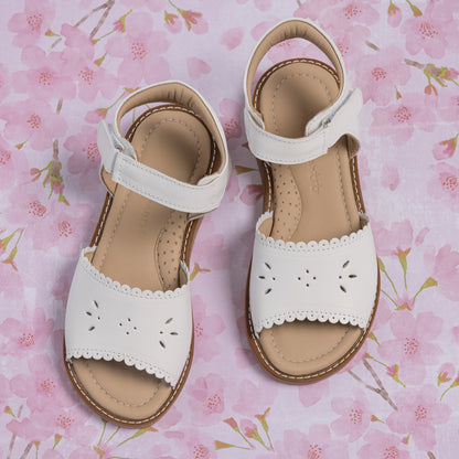 White toddler sandals with scalloped edges and perforated floral details, adjustable ankle strap.