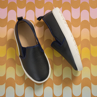 Black textured slip-on shoes for kids with white soles and pull tabs at the heel.