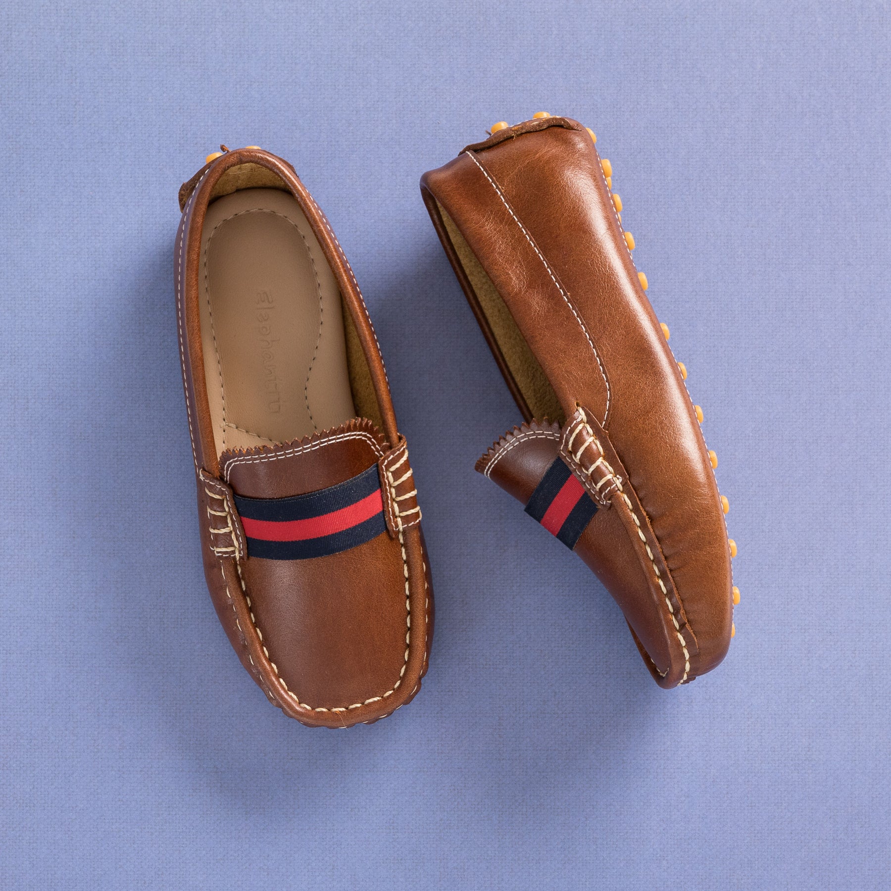 Natural brown leather toddler loafers with red and navy striped fabric band and moccasin stitching.
