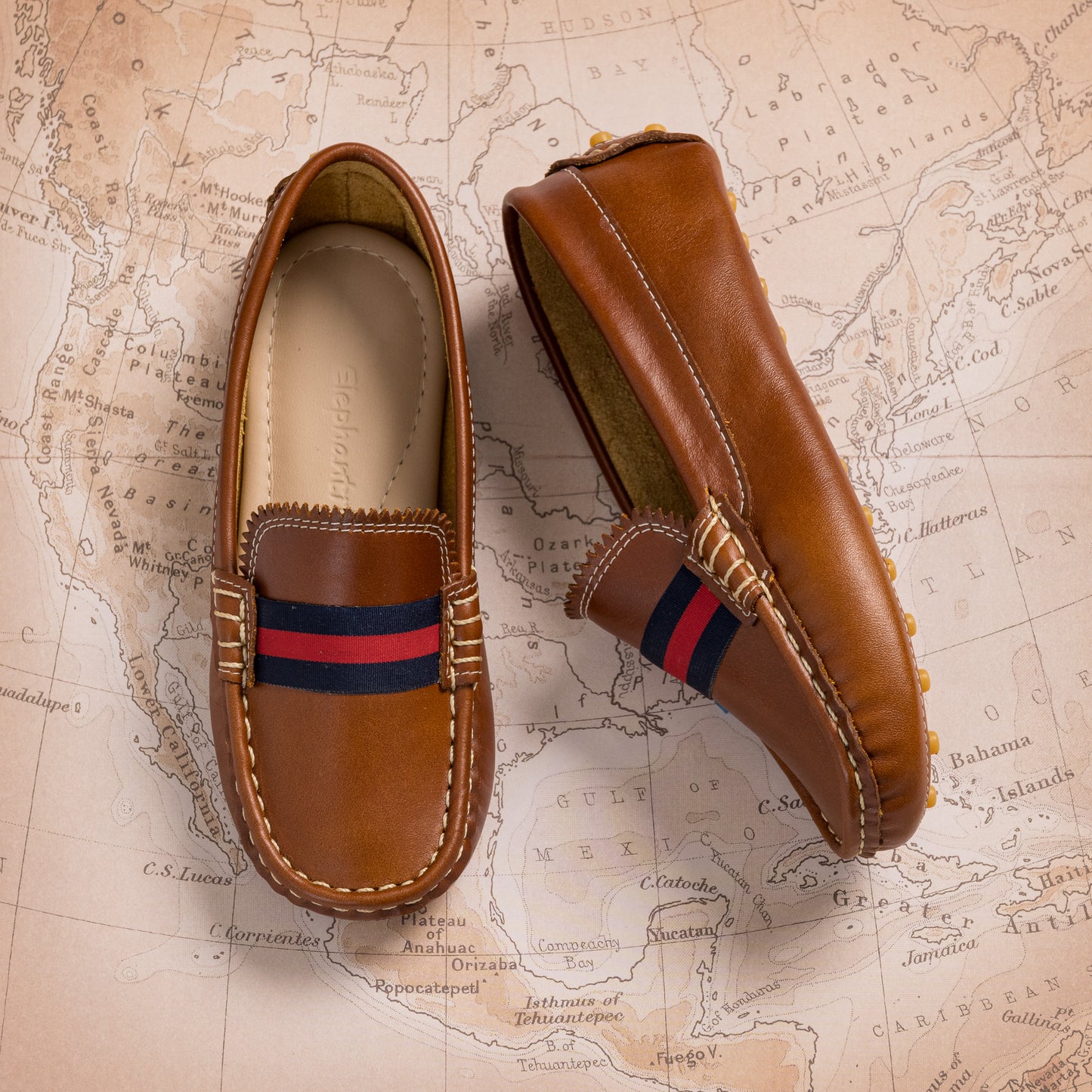 Natural brown leather baby loafer with navy and red striped fabric detail on top.
