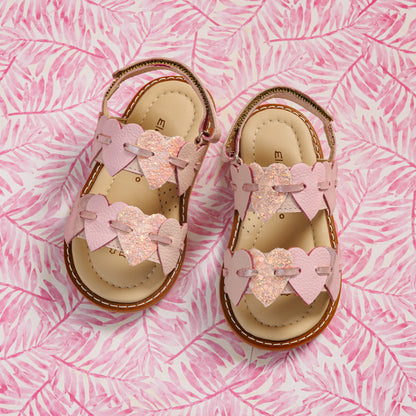 Elephantito - Pink toddler sandals with heart-shaped straps and cushioned tan insoles on a pink leaf-patterned background.