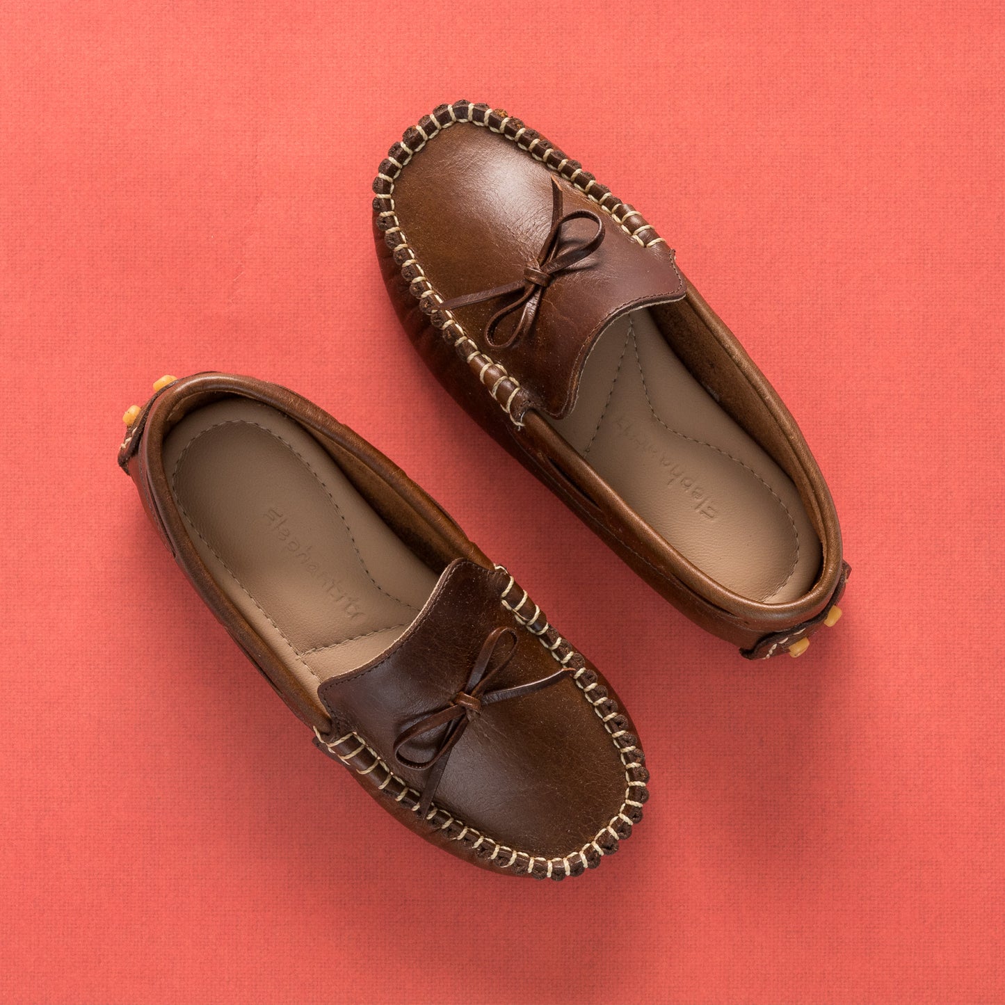 Brown leather boys' driver loafers with moccasin stitching and bow detail.