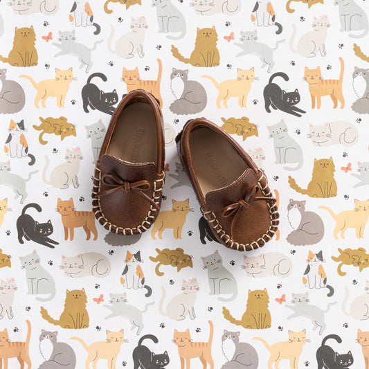 Brown baby driver loafers with leather bow and whipstitch detailing on sole edges.