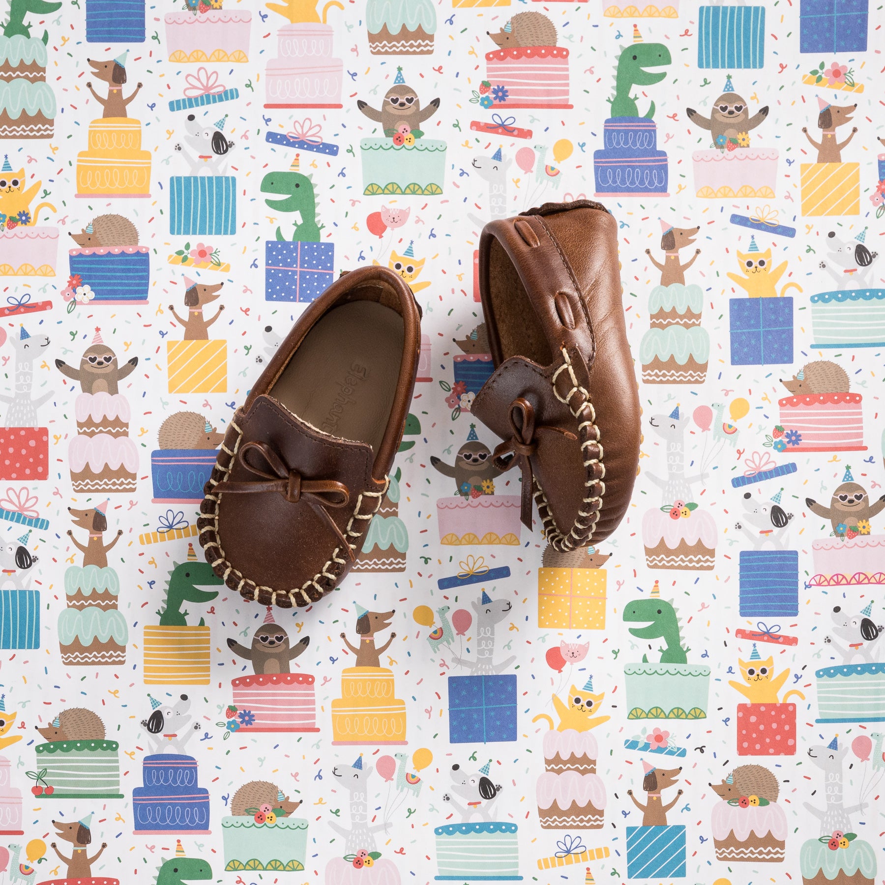 Brown leather baby driver loafers with front bow and woven detailing on rubber sole.