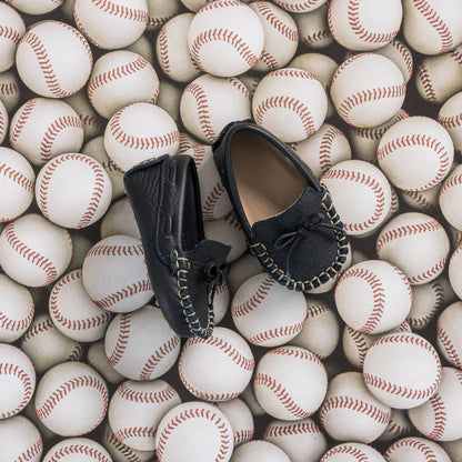 Navy blue baby driver loafers with black bow and stitching details on baseball background.