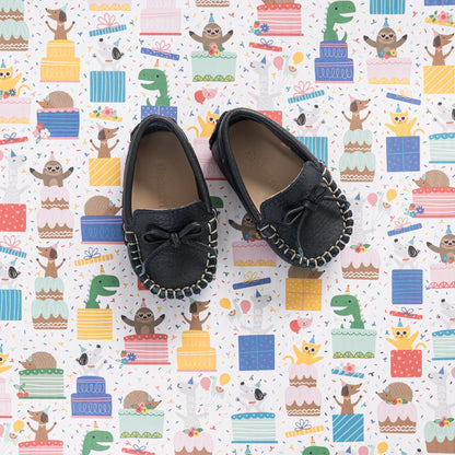 Navy blue baby driver loafers with bow detail and stitched trim on playful patterned background.