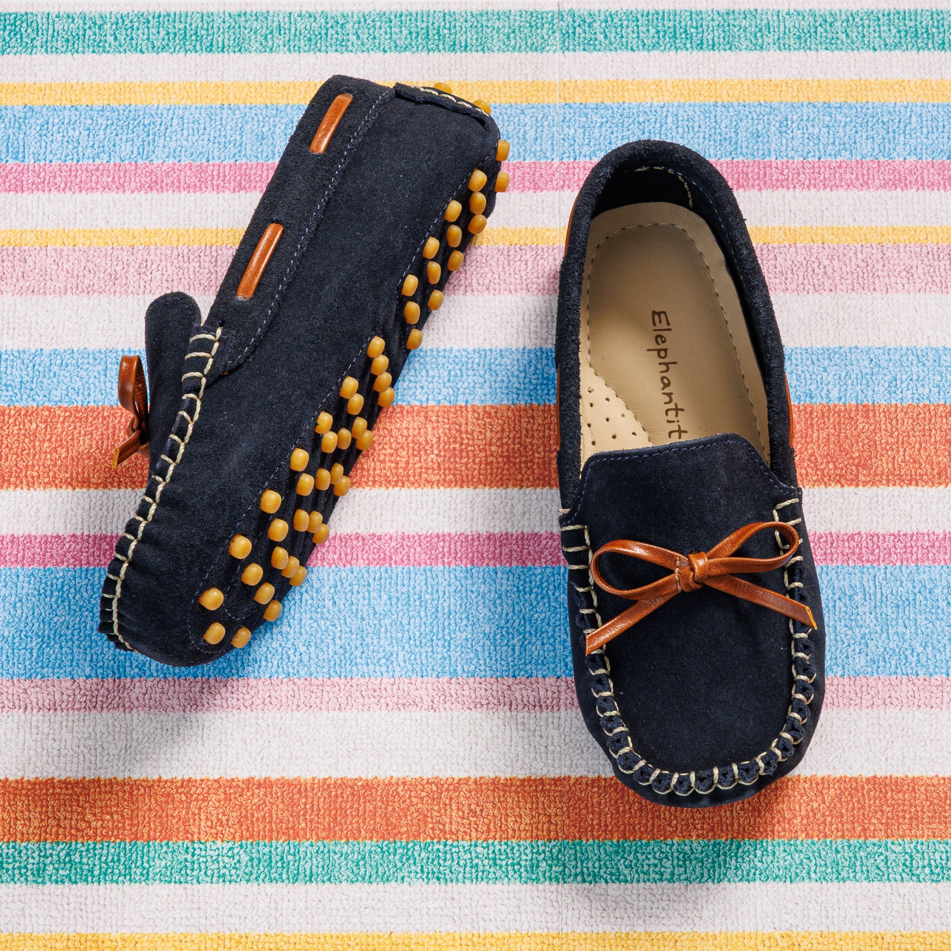 Elephantito - Navy blue suede kids' driver loafers with brown leather bow and yellow rubber sole grips on striped background.