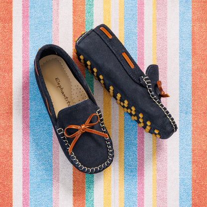 Elephantito - Navy blue suede boys' driver loafers with orange lace and yellow rubber sole grips on striped background.