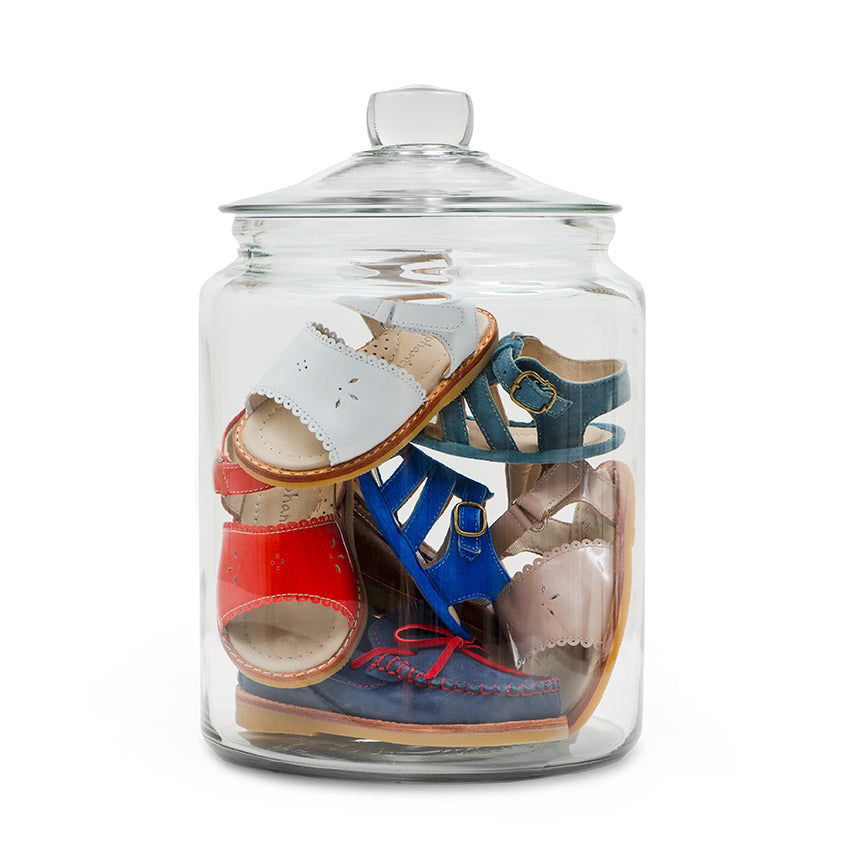 Clear glass jar filled with colorful toddler sandals in white, red, blue, and beige.