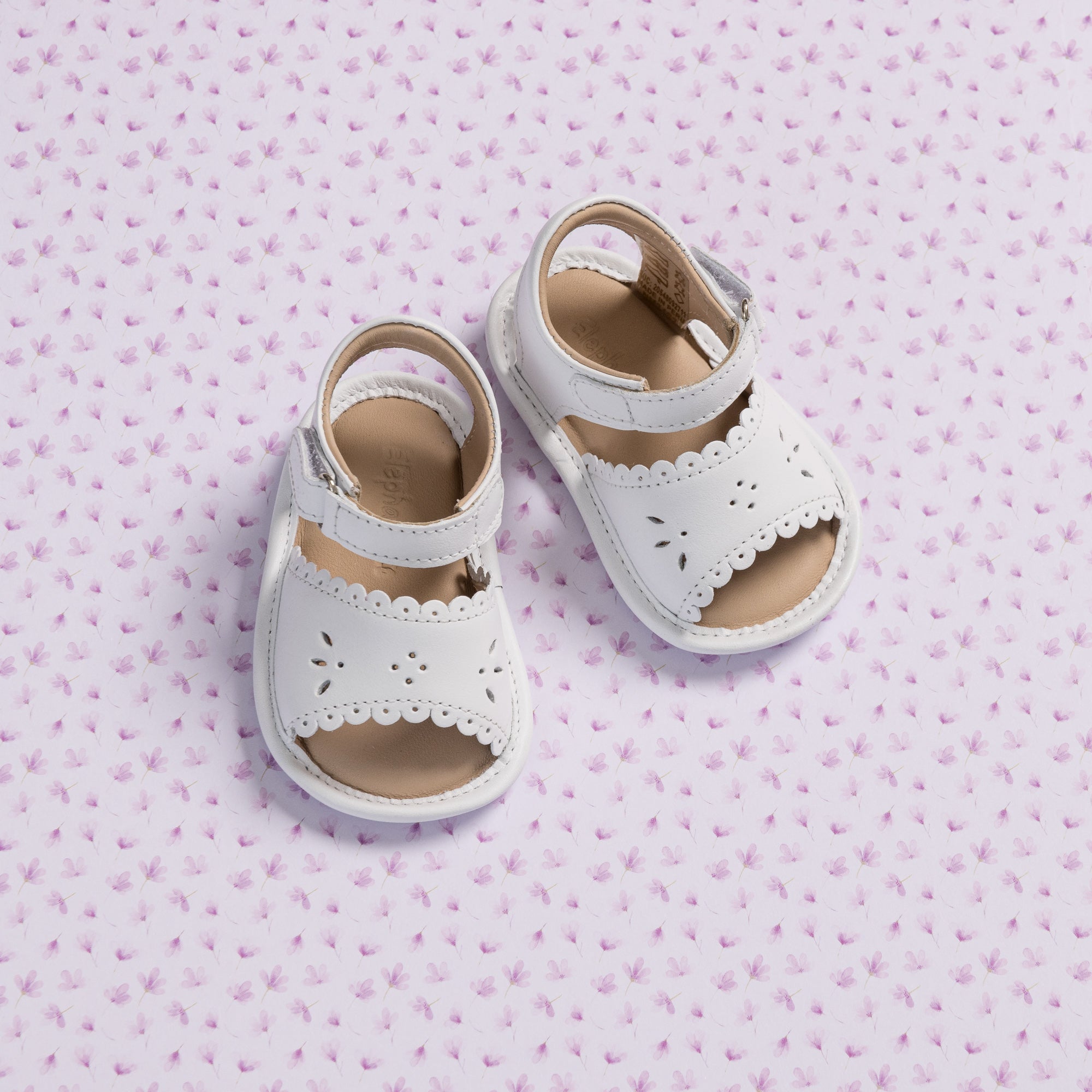 White baby sandals with scalloped edges and floral cutout details on soft leather uppers.