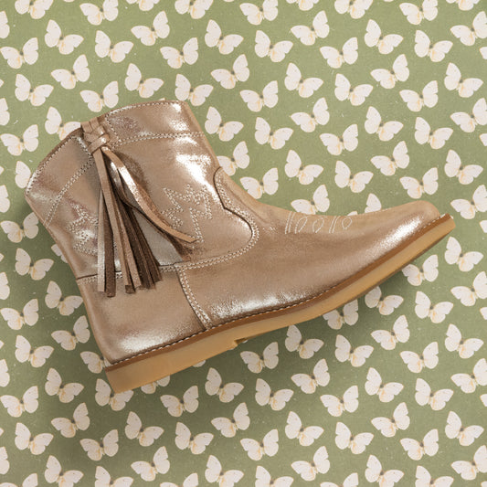 Metallic blush suede toddler boot with side tassels and stitched detailing on butterfly-patterned background.